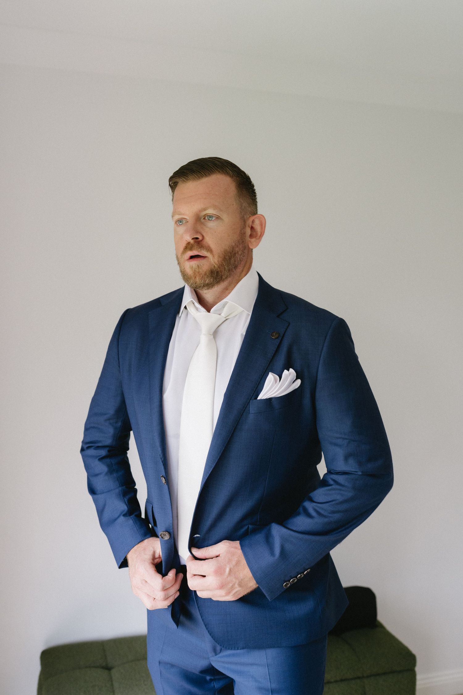 A person wearing a tailored navy blue suit with white shirt and pocket square.