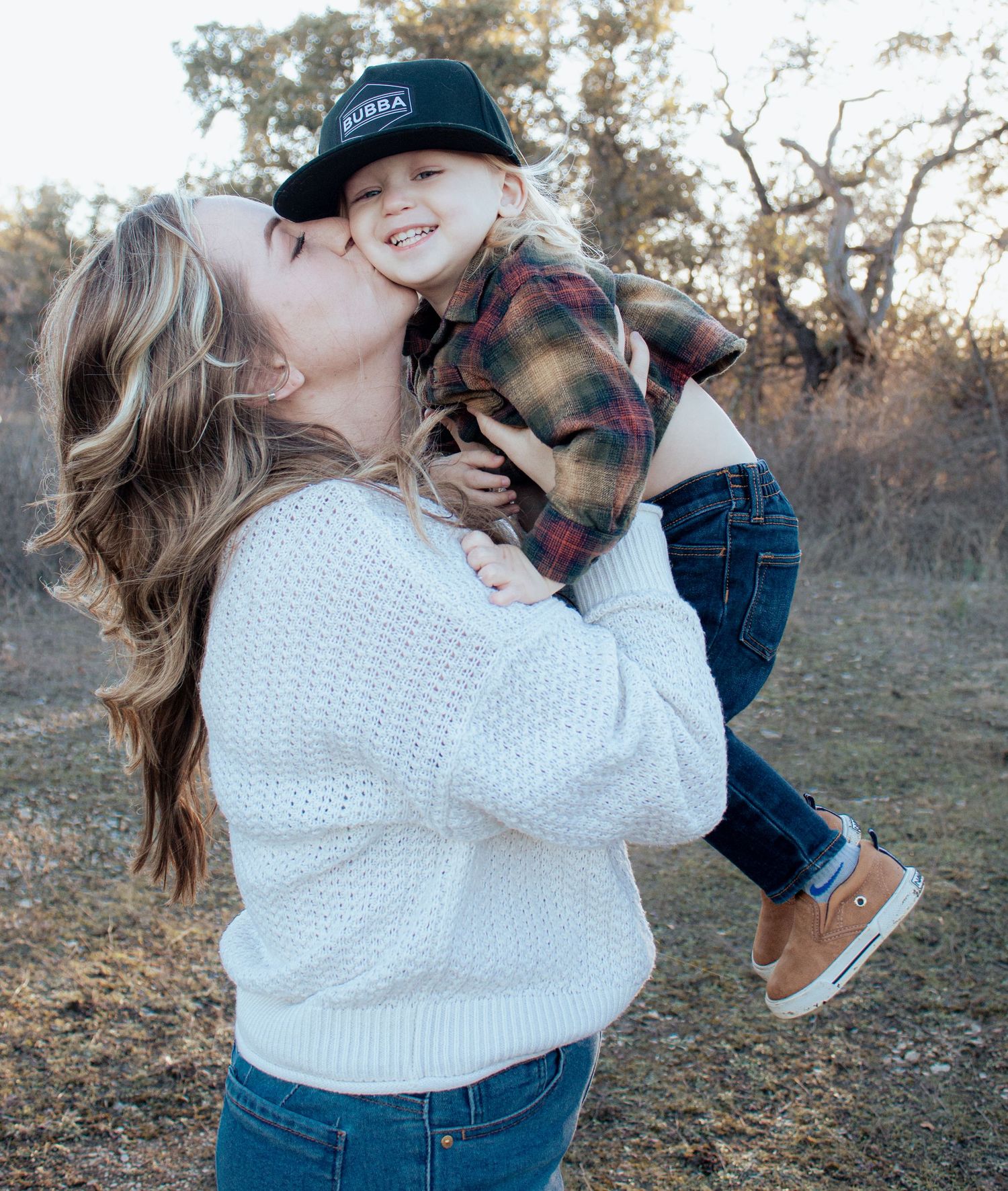 A heartwarming moment outdoors as a parent in a white knit sweater shares an affectionate moment with a child in plaid and cap.