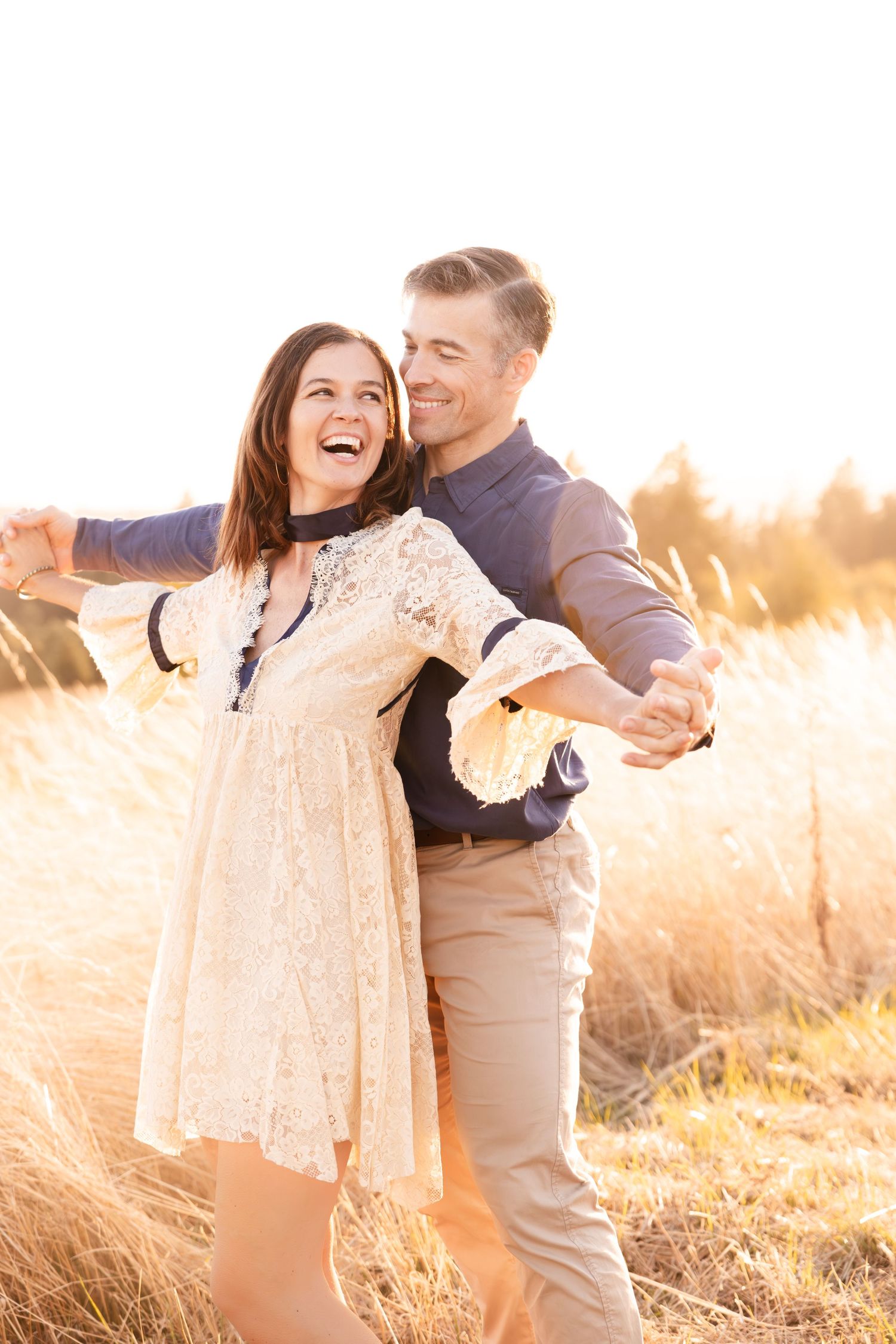 Joyful couple dancing in a sunlit field wearing casual elegant attire.