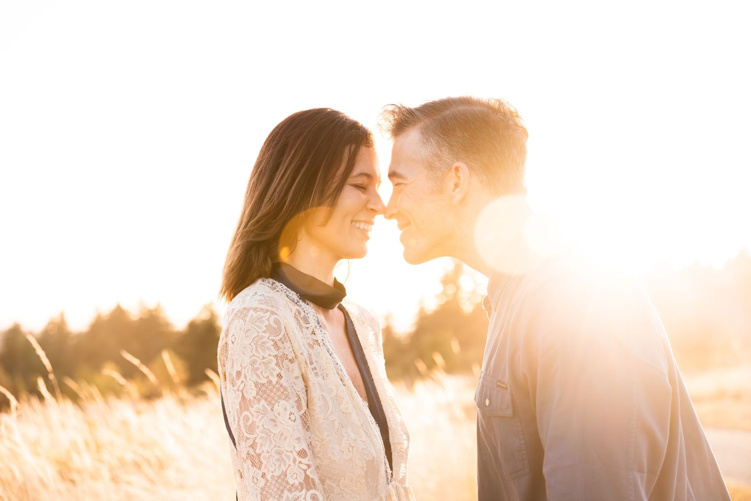 Couple sharing an intimate moment in warm sunlight with trees in background.