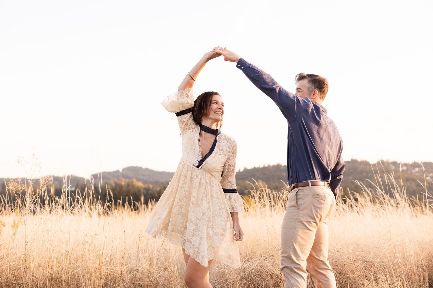 Couple dancing together in a golden grass field during sunset.