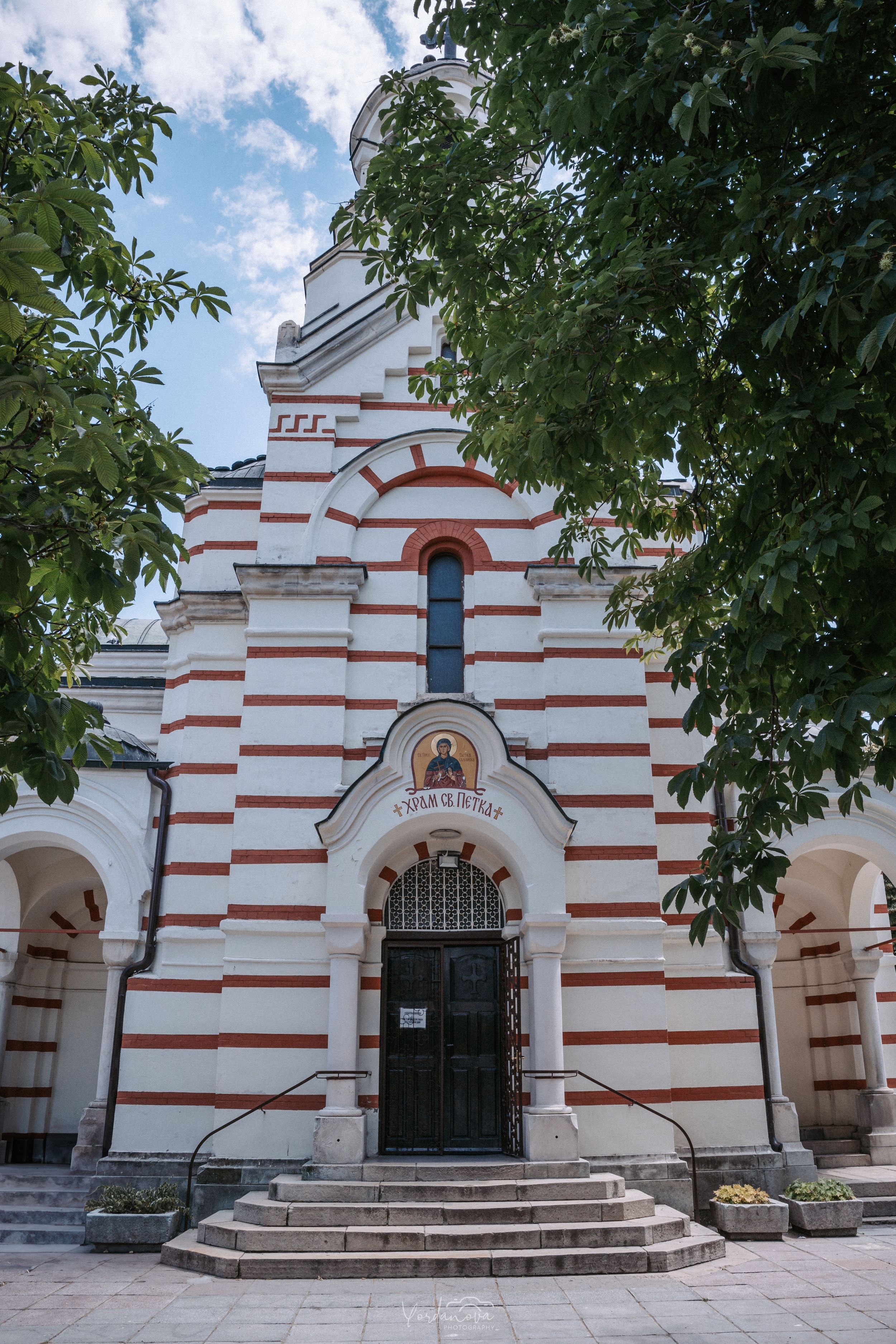 White orthodox church building with red striped architecture and arched entrance.