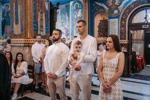 Family attending Orthodox ceremony in church with blue frescoed walls and golden details.
