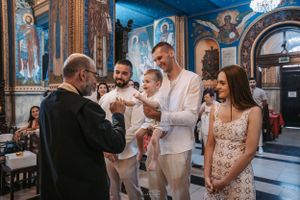 Orthodox baptism ceremony taking place in richly decorated church with blue and gold frescos.