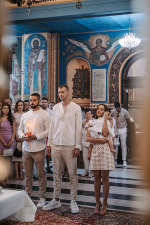 People attending Orthodox ceremony in church with beautifully painted walls and ceiling.