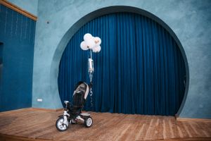 White balloons attached to a small tricycle against a blue curved archway.