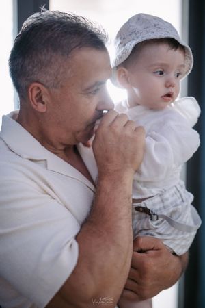 A tender moment between a man in white holding a small child in a light-colored outfit.