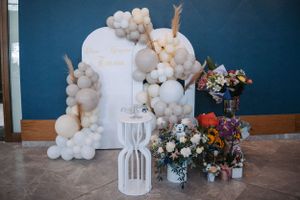 Elegant white balloon arch with floral arrangements against blue wall for special event.