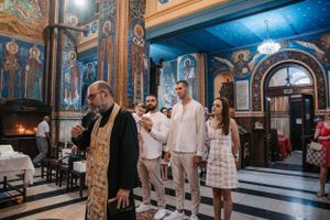 Orthodox church interior with religious ceremony and ornate blue and gold frescoed walls and ceiling.