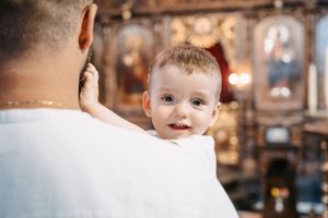 Small child looking over someone's shoulder inside an ornate Orthodox church.