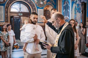 Orthodox priest performing religious ceremony with attendees in an elaborately decorated church.