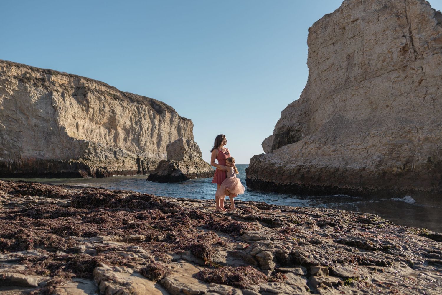 Mother and daughter standing on seaside rocks near ocean and rock cliffs on Maui