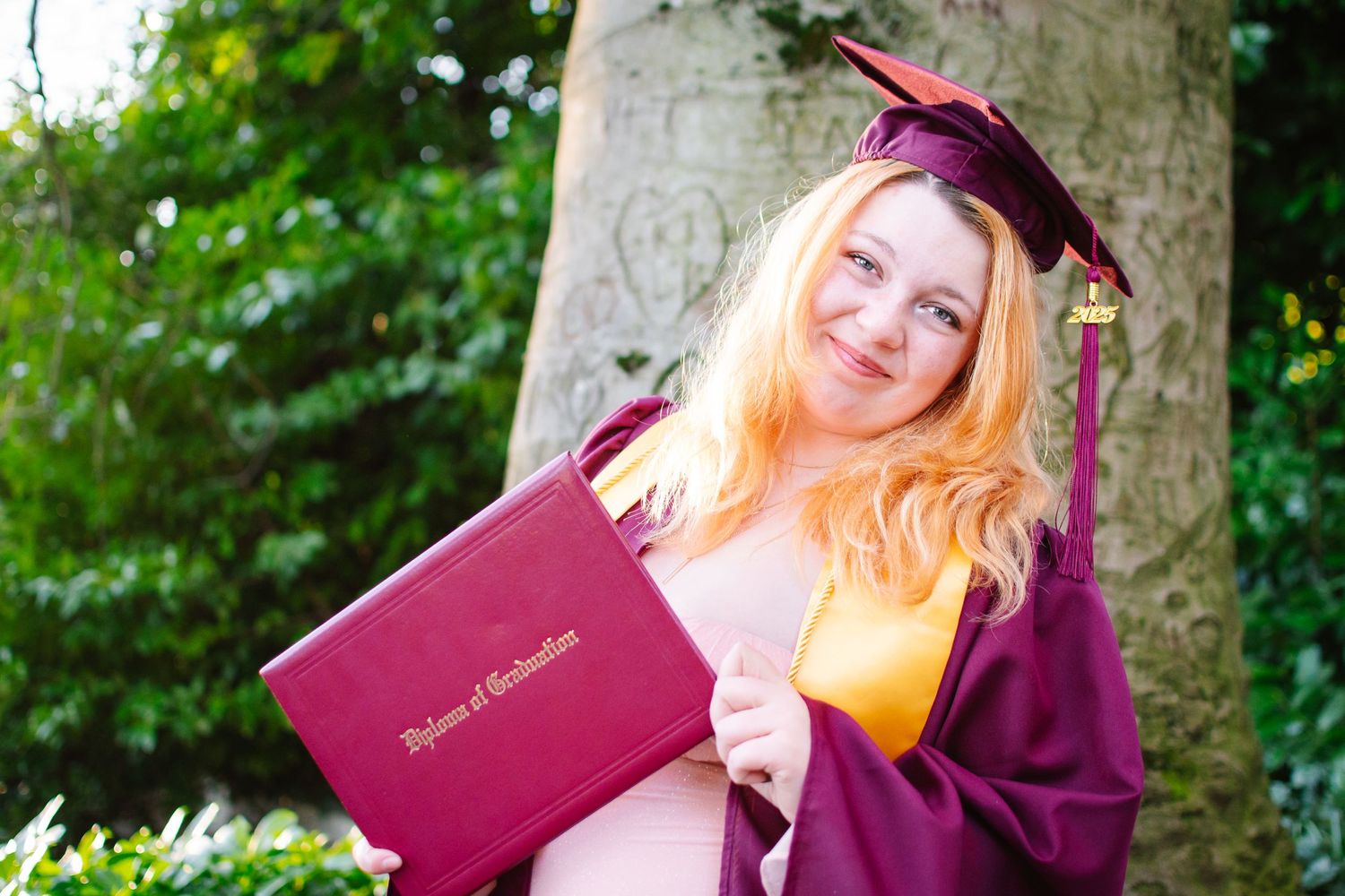 Senior photo of graduate in cap and gown proudly holding diploma in front of tree at Kerry Park in Seattle.