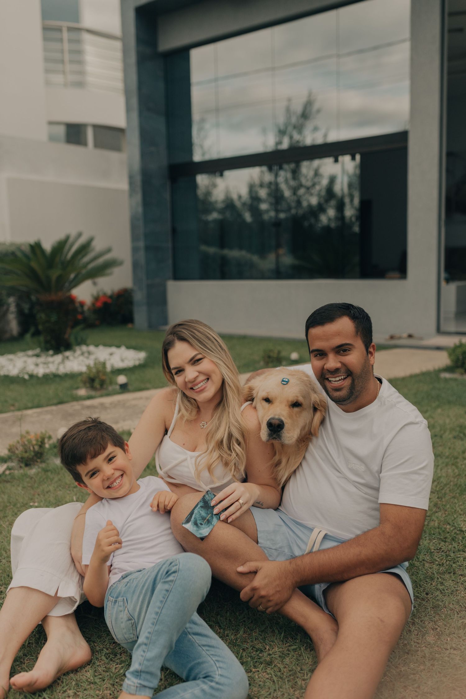 Family sitting on lawn with golden retriever in front of modern house.