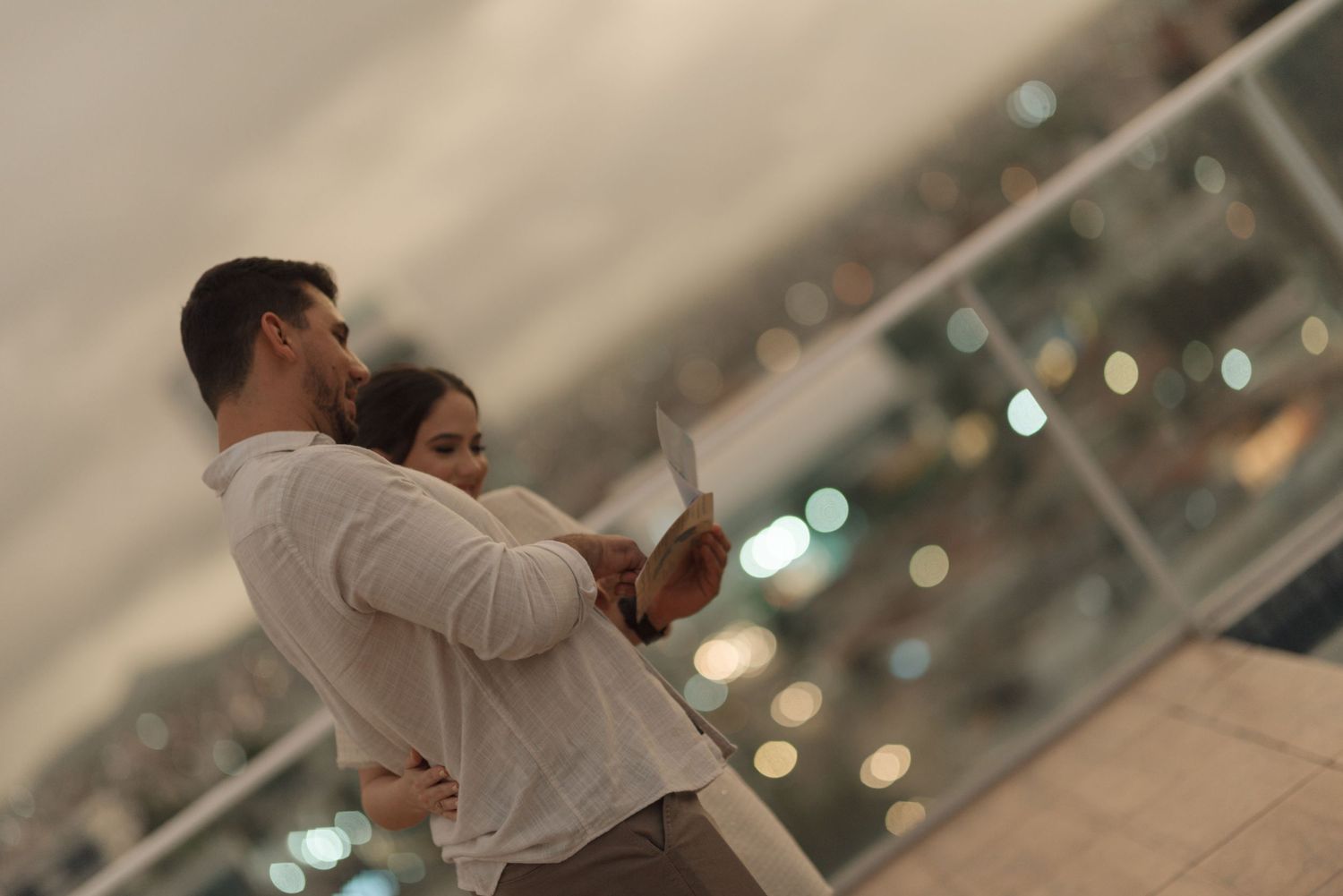 A tender moment captured against city lights in soft focus during a pregnancy announcement.