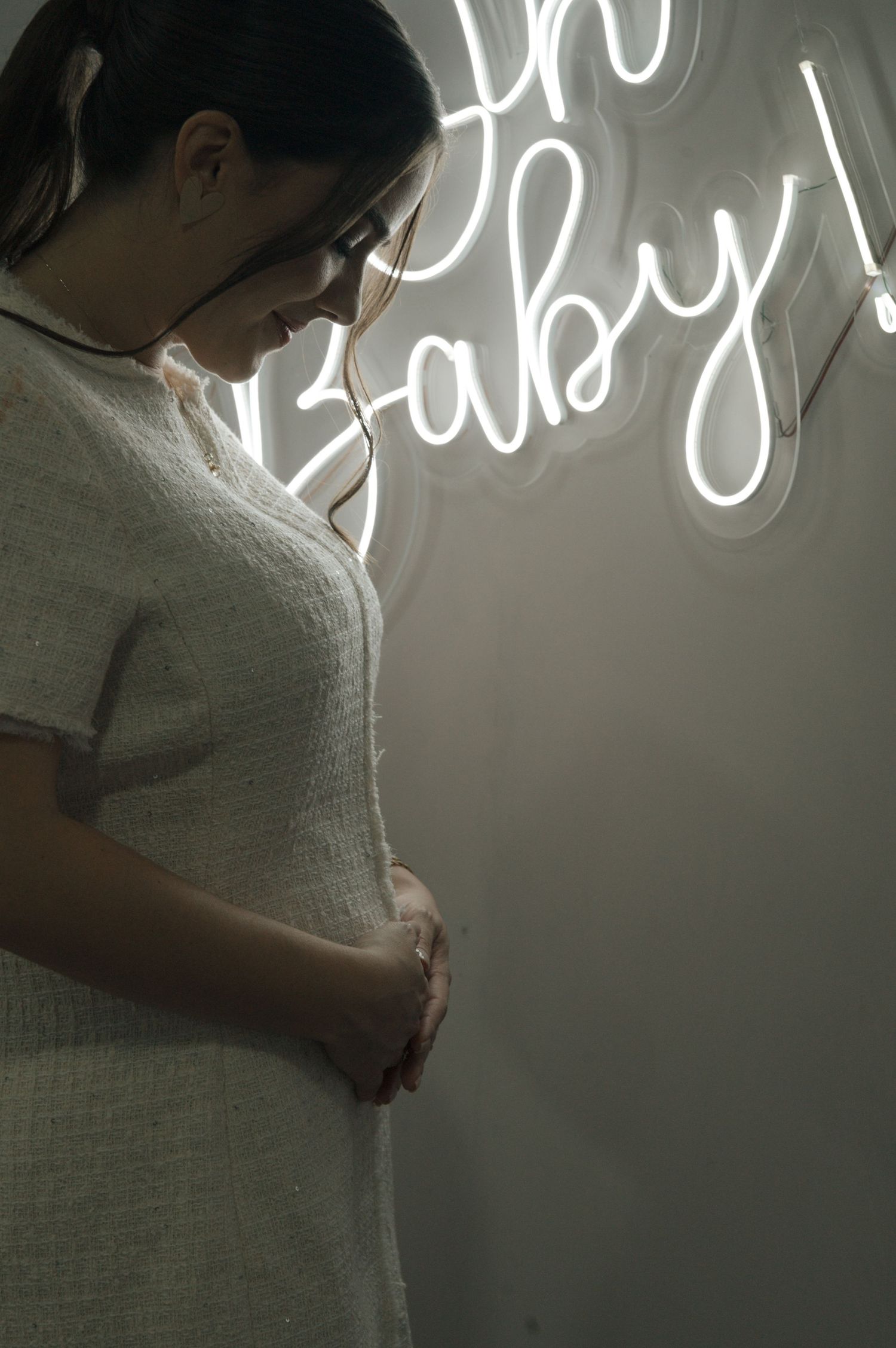 A silhouette of an expectant mother standing beside a glowing neon 'Baby' sign.