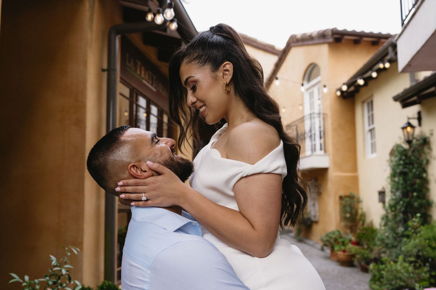 A tender moment between a couple against a Mediterranean-style building backdrop.