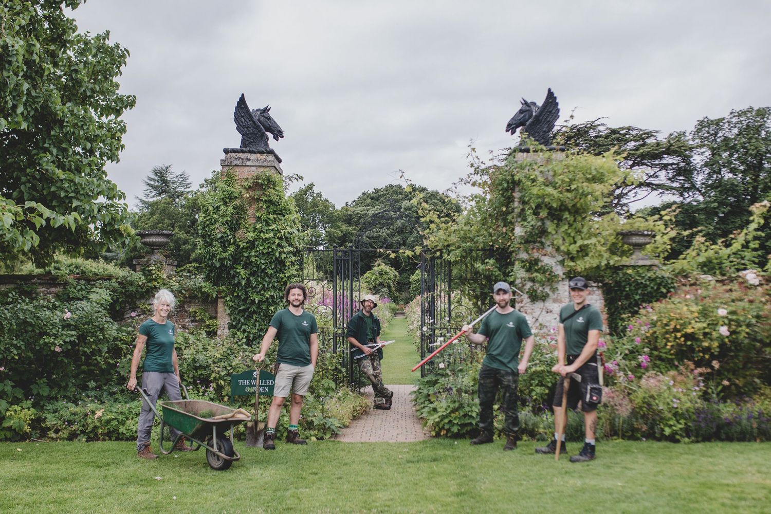 Group of gardeners gathered in a garden with equestrian statues visible in background.