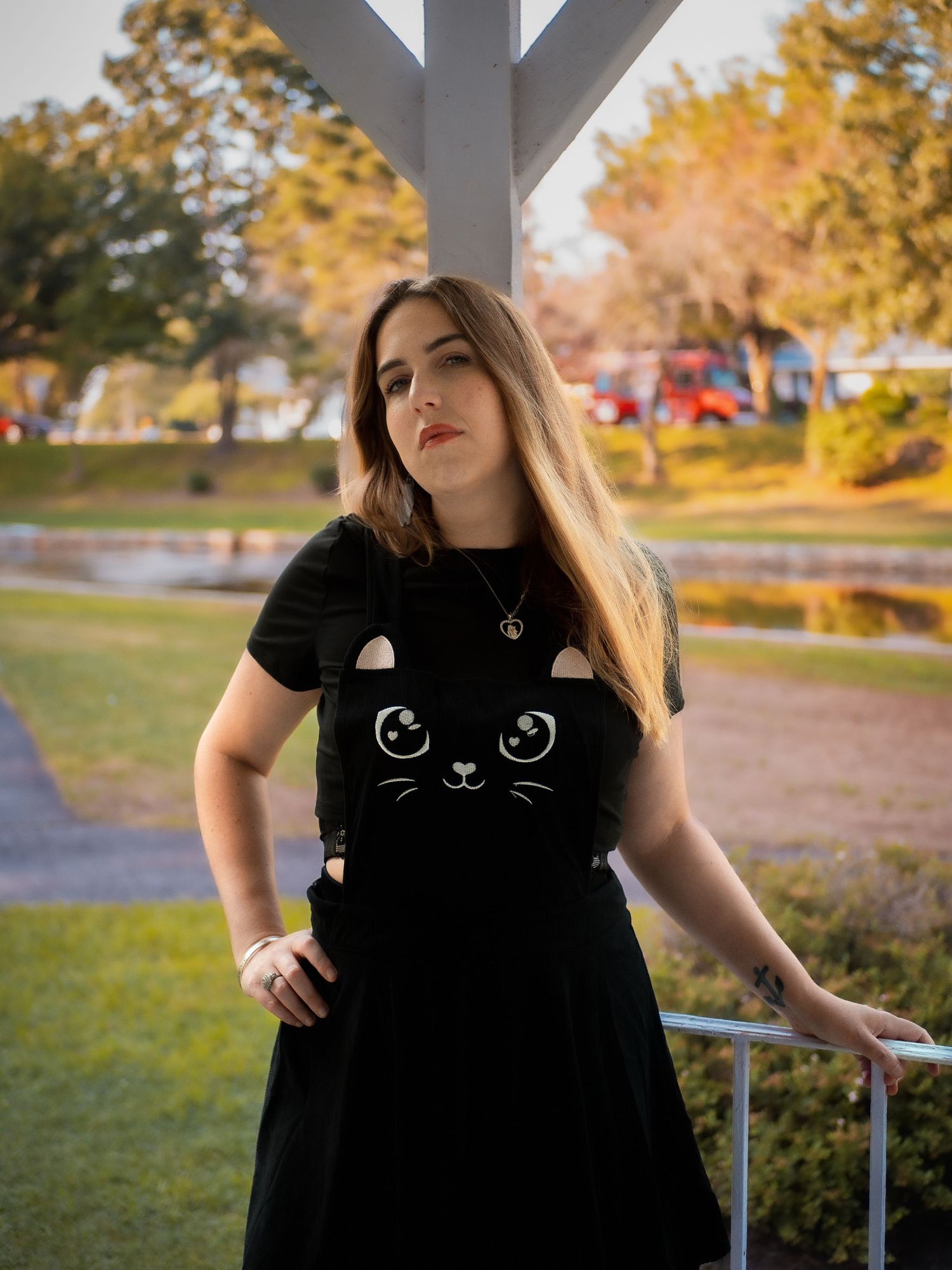 A person wearing a black cat t-shirt dress poses outdoors against an autumn backdrop with golden foliage.