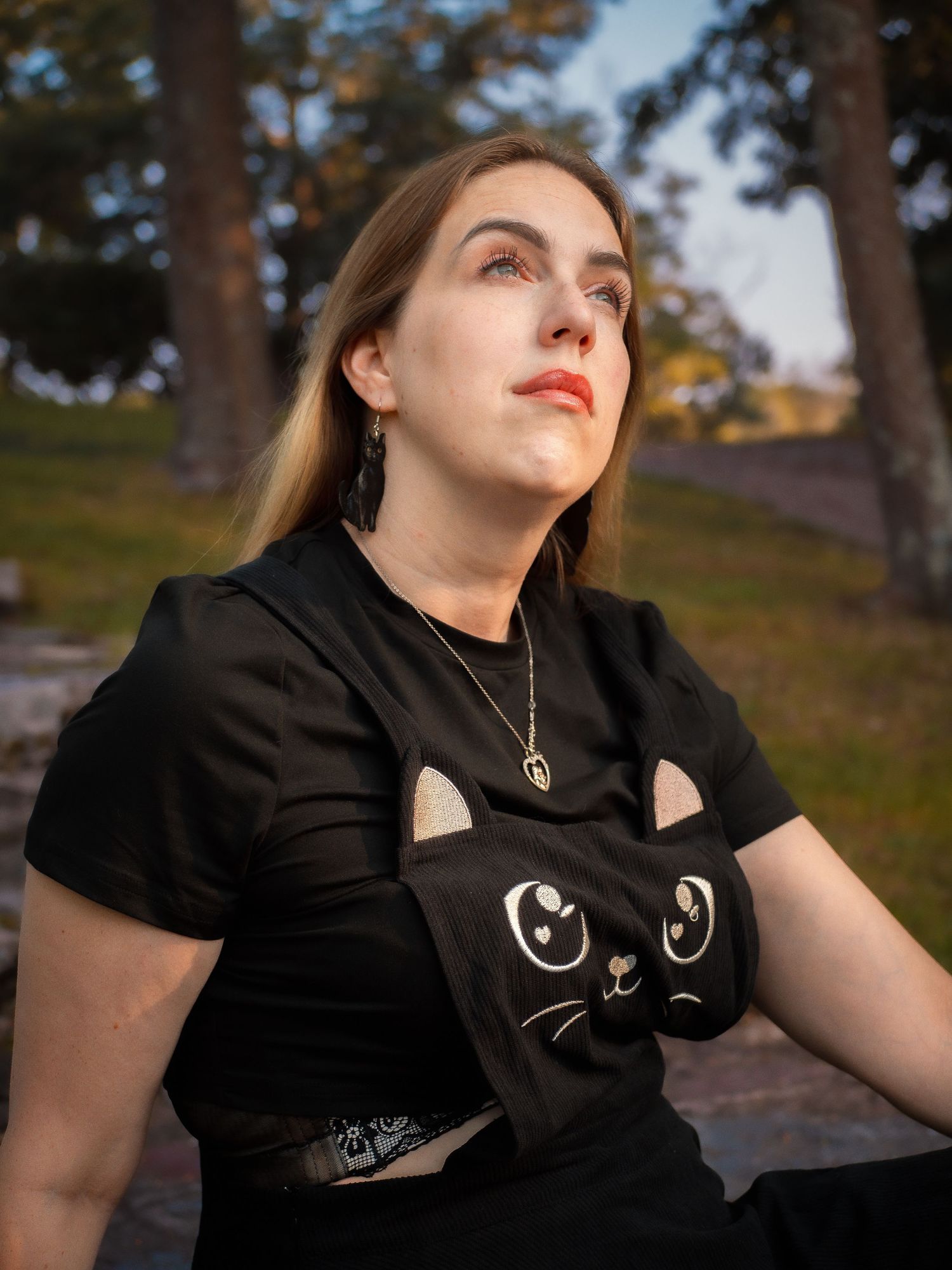Person wearing black t-shirt with cute cat face design sitting outdoors at sunset in natural setting.