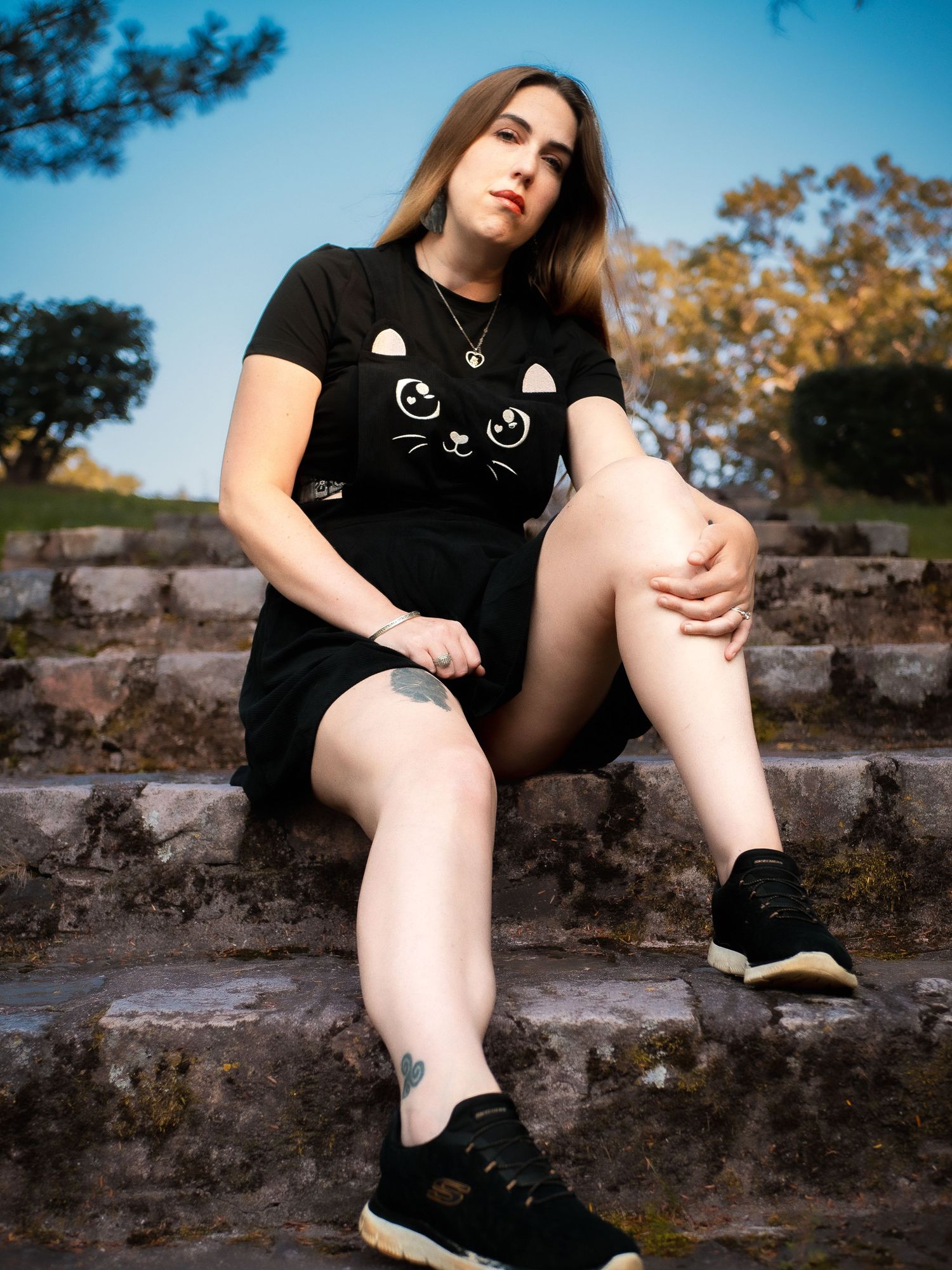 Person wearing a black cat graphic t-shirt sits on stone steps outdoors on a sunny day.
