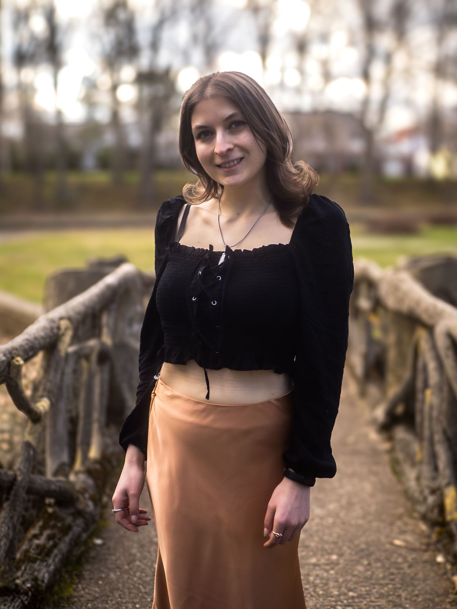 Portrait on a rustic wooden bridge featuring a black cropped sweater paired with a peach colored maxi skirt.