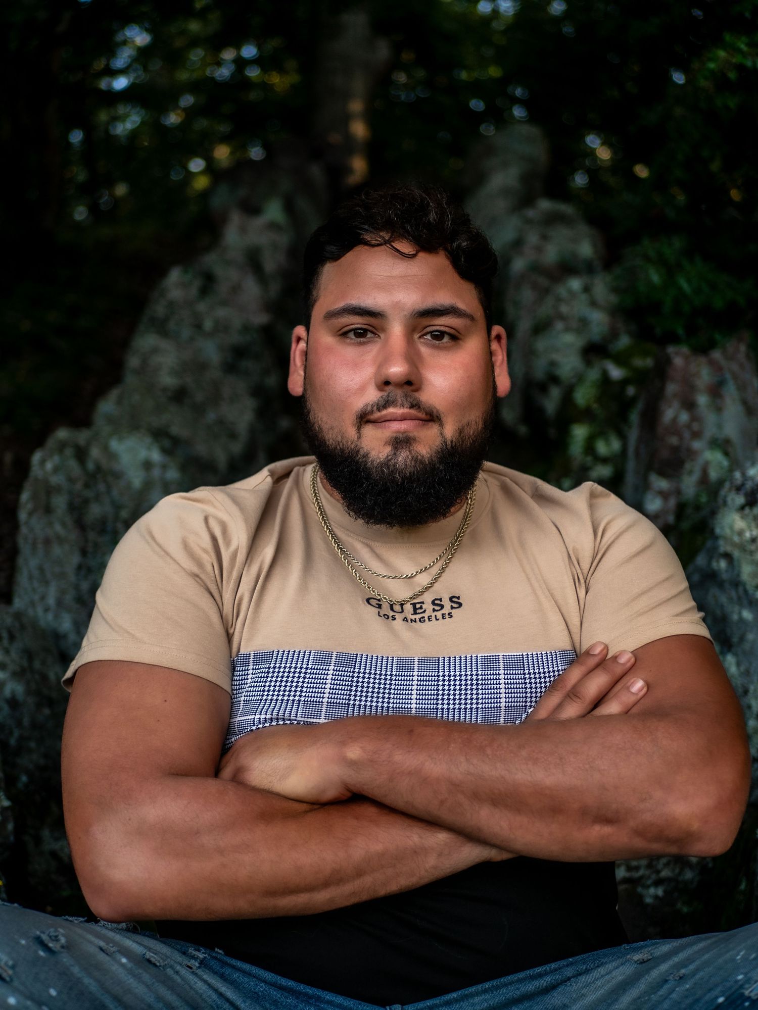 A person in a color block t-shirt poses with crossed arms against a rocky outdoor backdrop.