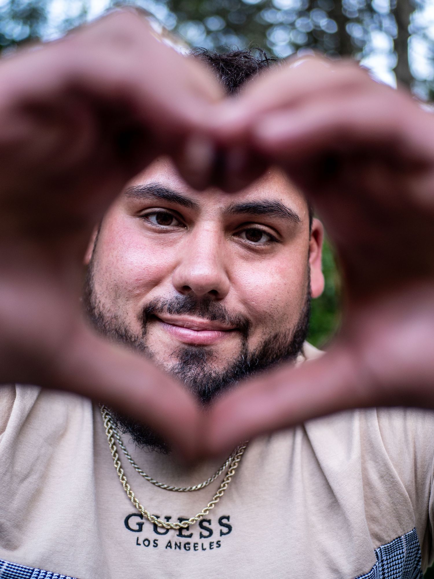 A creative portrait showing someone framing their face with a heart shape made from hands in front of trees.