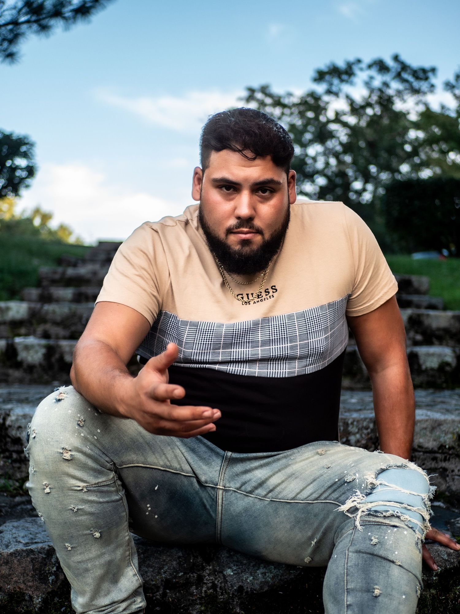 Urban fashion portrait on stone steps featuring casual wear with a tri-color t-shirt and ripped jeans.