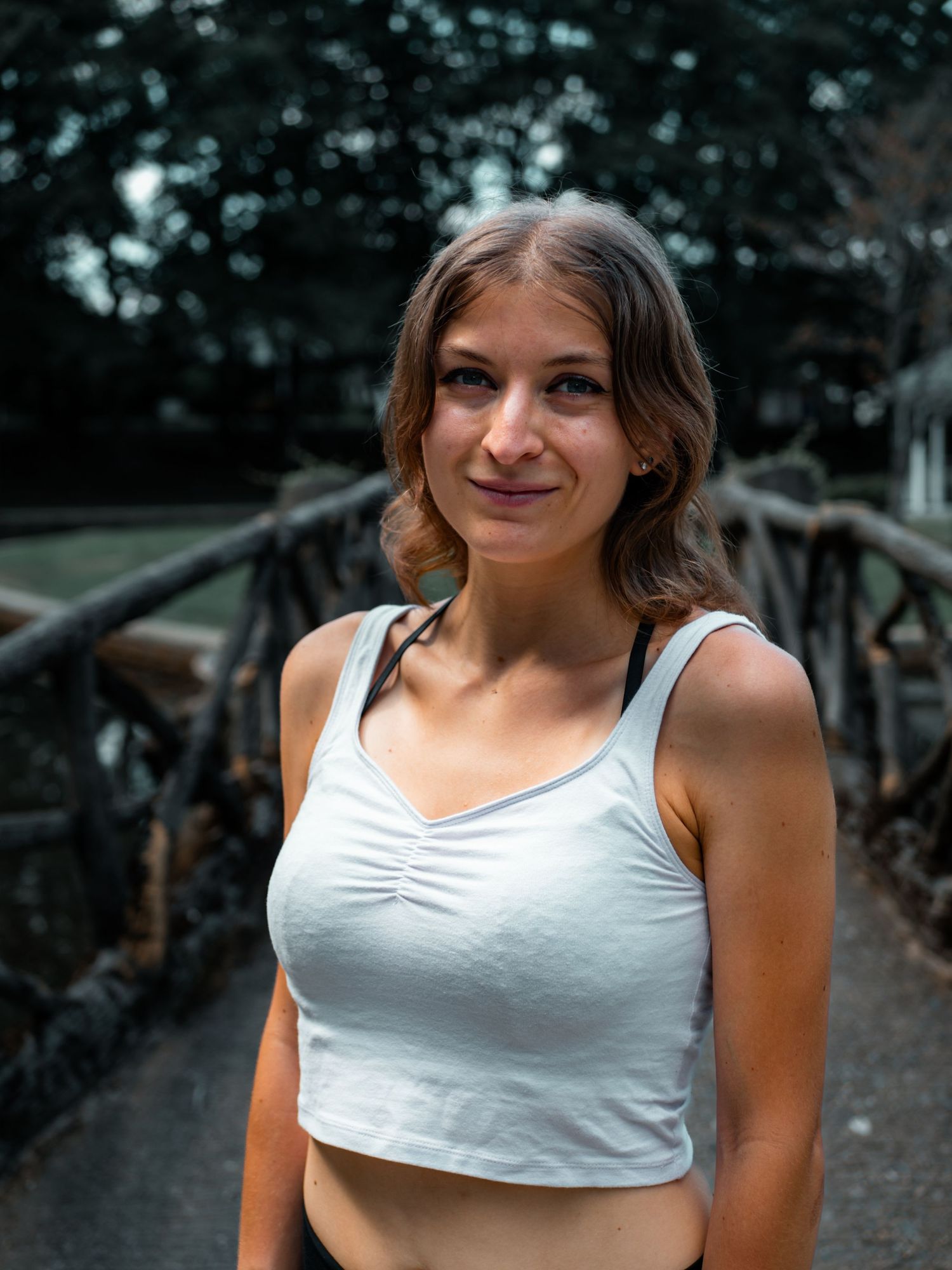 Someone wearing a white crop top smiles while posing outdoors against a leafy green background.