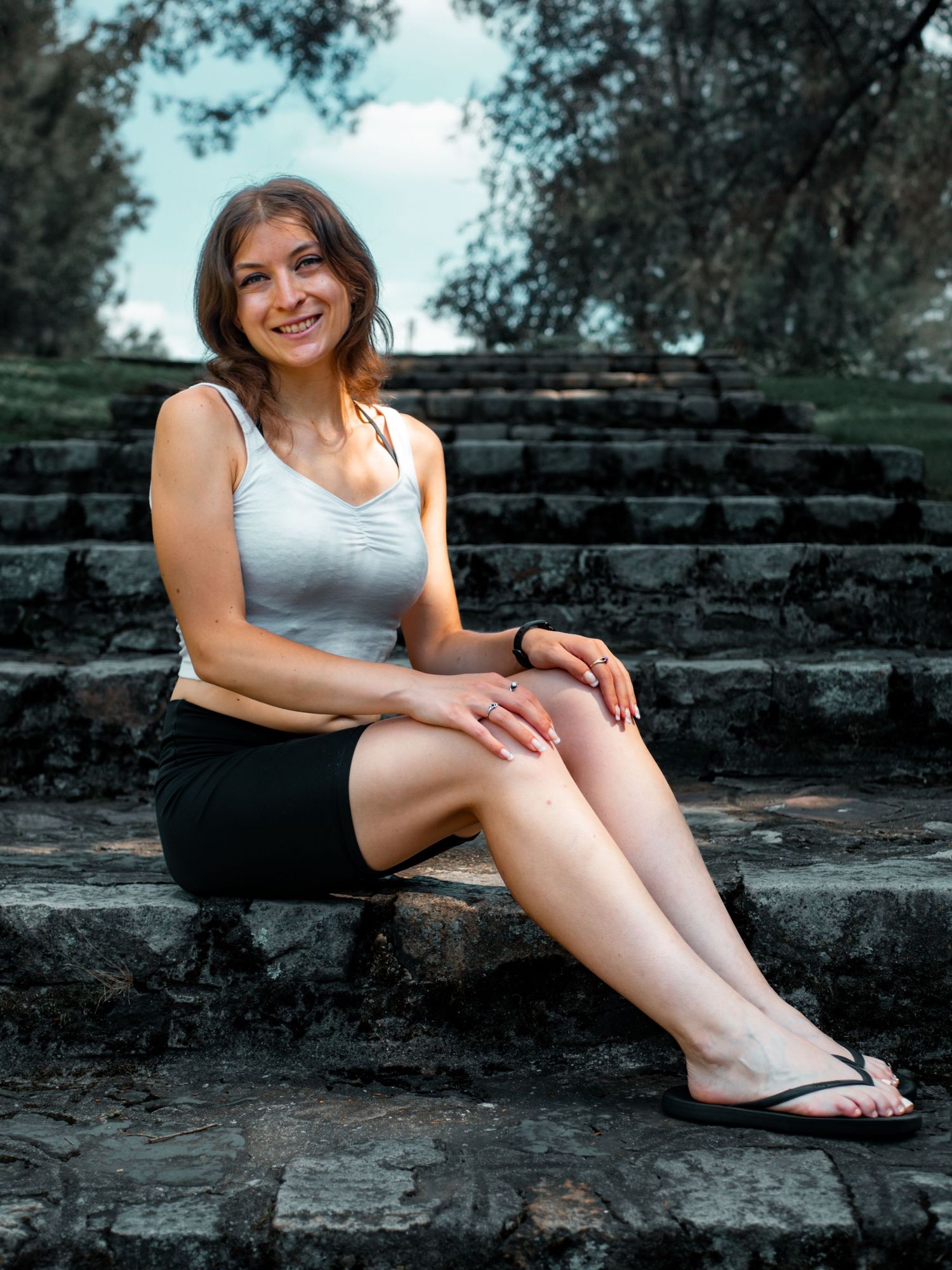 A casual outdoor portrait of someone sitting on stone steps surrounded by lush greenery.