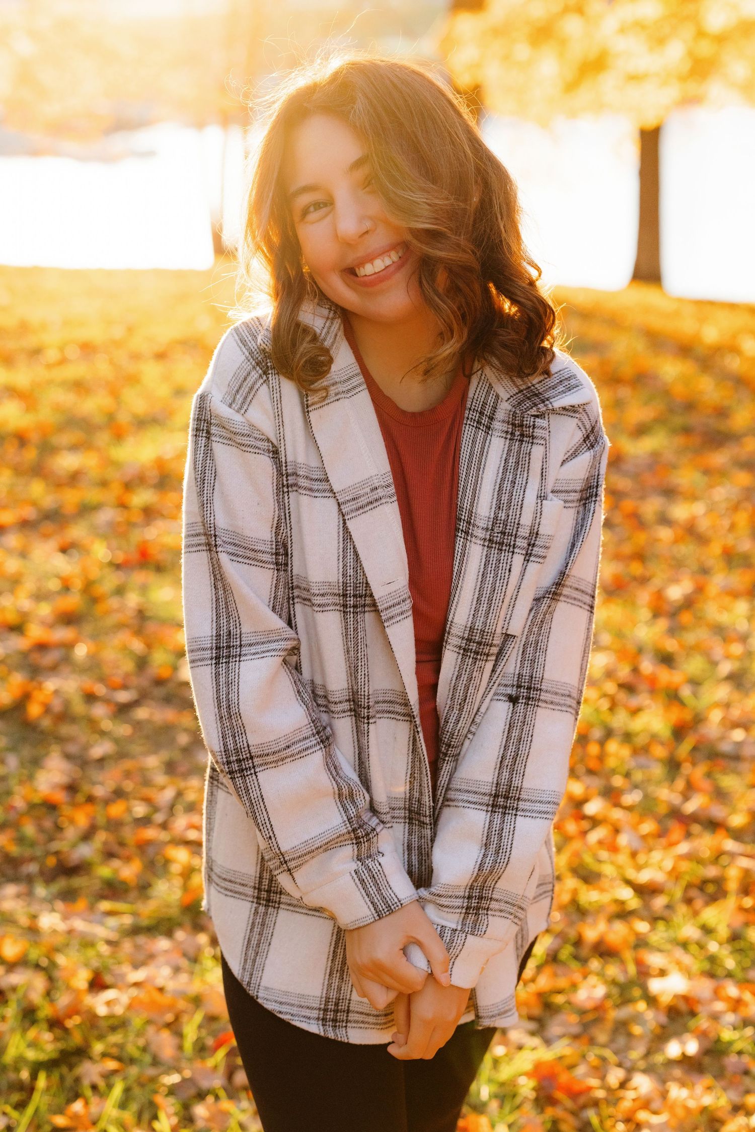 Cozy autumn portrait with plaid flannel shirt and warm sunlight filtering through fallen leaves in a park.