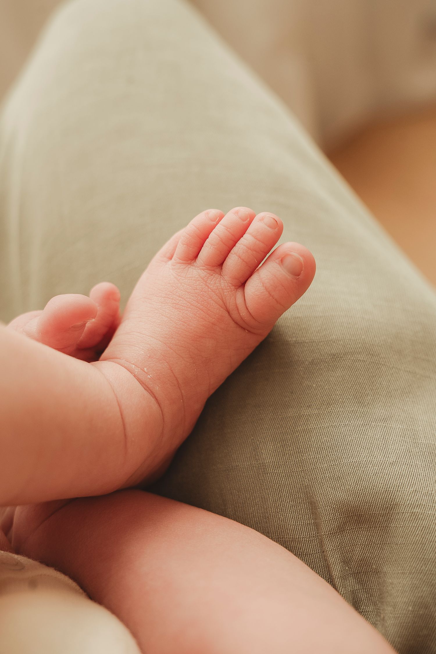 Close up of tiny baby feet and legs resting on a beige cushion or pillow.