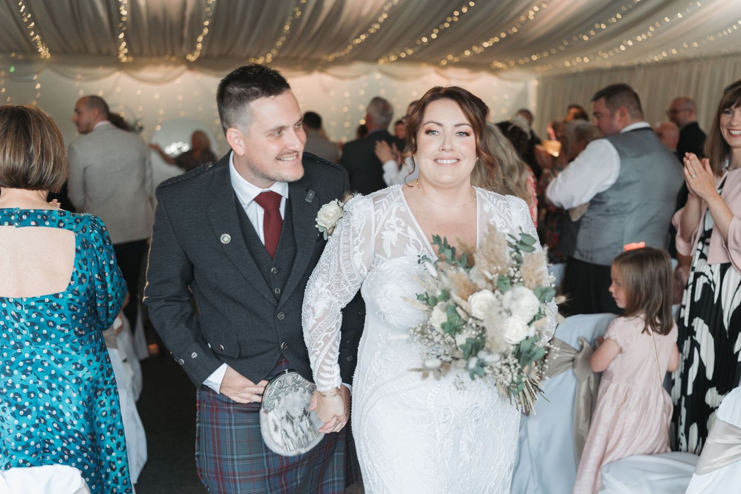 A joyful couple at an elegant wedding ceremony inside a reception venue with twinkle lights overhead.