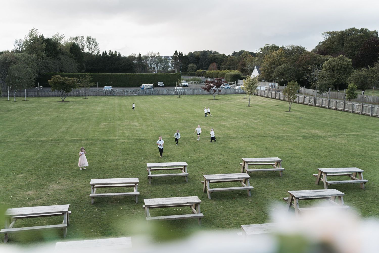 Empty bleachers line a grassy sports field where players practice on a sunny afternoon.