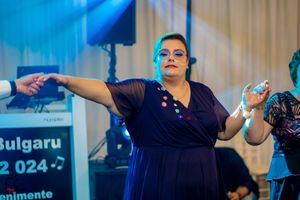 Woman in navy dress dancing energetically at an indoor event with Bulgarian text visible.