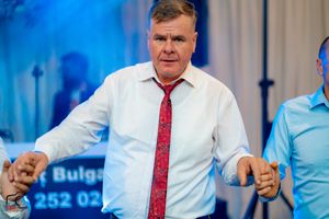 Guests dancing at a formal event with blue lighting and Bulgarian text visible in the background.