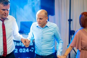Three people holding hands while dancing at an event with blue lighting.