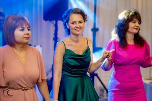 Three women in elegant dresses dancing together at an event.