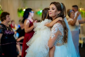 A bride in a lace dress holds a small child wearing white at a wedding reception.