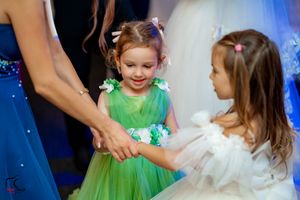 Children in formal attire dance and twirl at a wedding reception with blue lighting effects.