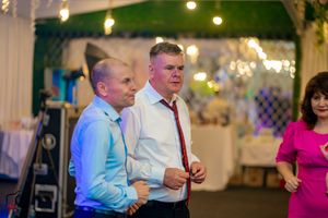 Indoor celebration with guests dancing under atmospheric lighting and green foliage decor.