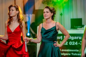 Dancers in red and green dresses perform at an event with colorful stage lighting.