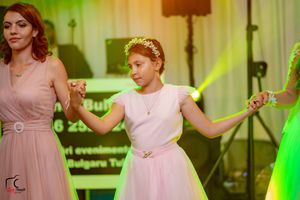 Wedding party dancing together at a reception with colorful green lighting and white curtains in the background.