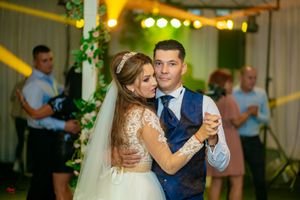 A couple dancing at their wedding reception with yellow lights and greenery decorating the venue.
