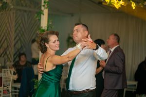 A couple dancing together at an evening event, with the woman wearing an emerald green dress.