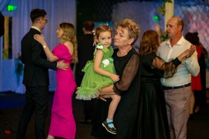 People dancing at a formal event with someone in a bright pink dress and a child in green.
