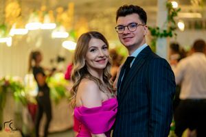 Elegantly dressed couple posing at a formal event with decorative lighting in the background.