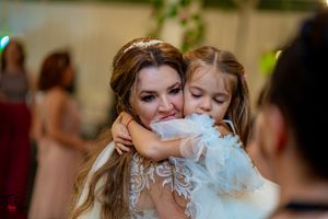 Emotional wedding moment captured between bride and young girl hugging at reception.
