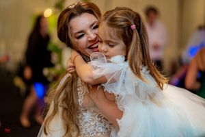 A tender moment shared between a bride in lace and a young girl in white at a wedding reception.
